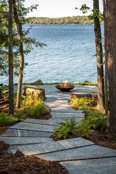 a stone path leading to a lake with trees around it and a fire pit in the middle