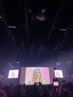 a large screen with a woman on it in the middle of a crowd at a concert