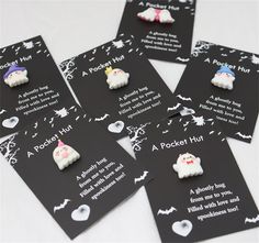 four little ghost pins are sitting on top of black cards with white writing that says pocket hug