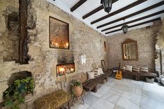 a room with stone walls and wooden benches in the center is filled with candles, plants, and pictures on the wall