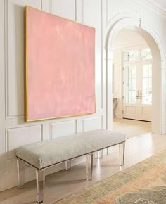 a large pink painting hangs on the wall above a bench in an elegant entryway