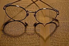 a pair of glasses sitting on top of an open book with the shadow of a heart