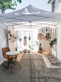 a white tent with plants hanging on the wall and a table in front of it