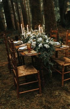 a table set up with candles and flowers on it in the middle of a forest