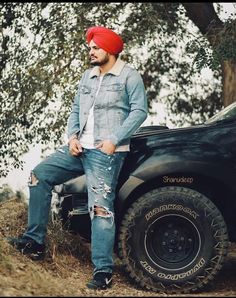 a man sitting on the back of a truck wearing a red beanie and jeans