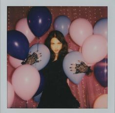 a woman standing in front of balloons with her hands on the ballons that are blue and pink