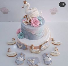 a three tiered cake with swans and flowers on the top is surrounded by cookies