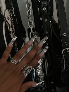 a woman's hand with long nails and rings on her fingers next to several purses