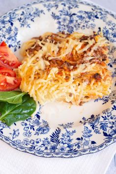 a blue and white plate topped with pasta and veggies next to a slice of tomato