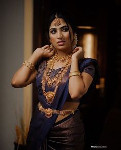 a woman in a blue sari with gold jewelry on her neck and hands behind her head