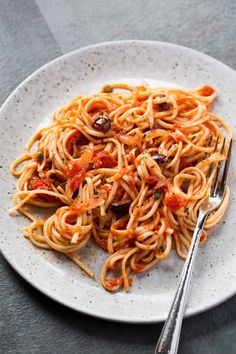 a white plate topped with pasta covered in tomato sauce and olives next to a fork