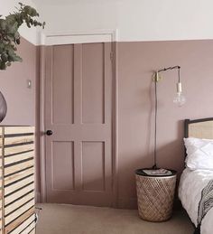 a bedroom with pink walls and white bedding is pictured in this image, there is a plant on the dresser next to the door