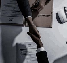 two people shaking hands over papers on a desk with mouses and other office supplies