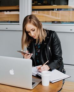 a woman sitting at a table with a laptop and pen in her hand while looking at the screen