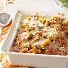 a white casserole dish filled with pasta and spinach on a table next to utensils