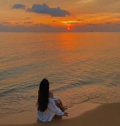 a woman sitting on the beach watching the sunset