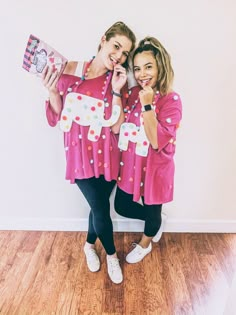 two women standing next to each other in front of a white wall holding up signs