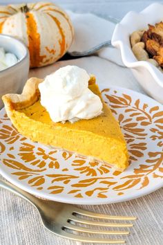 a slice of pumpkin pie with whipped cream on top sits on a plate next to other dishes