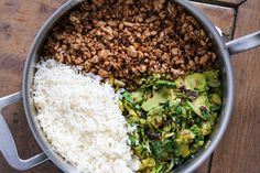 rice, meat and vegetables in a pot on a wooden surface with spoons next to it