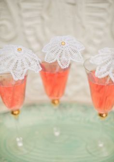 three glasses filled with pink liquid on top of a green tray next to a white doily