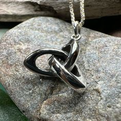 a silver necklace with two intertwined links on top of a rock next to water