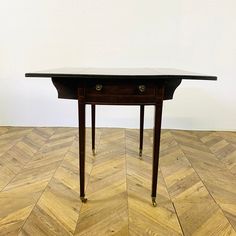 a small wooden table sitting on top of a chevron wood flooring covered in white walls