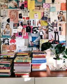 a bunch of books are stacked on top of each other in front of a wall covered with pictures