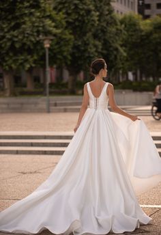 a woman in a white wedding dress leaning against a stone wall and looking at the street