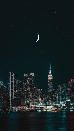 the city skyline is lit up at night, with a crescent moon in the sky