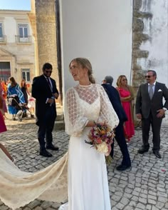 a woman in a wedding dress standing on a cobblestone street with other people