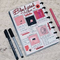 an open notebook with pink and black items on the cover, along with two pens