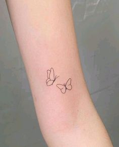 a small black butterfly tattoo on the left inner arm, with two smaller butterflies behind it