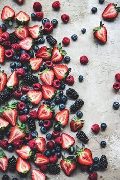 strawberries, blueberries and raspberries are arranged on a table