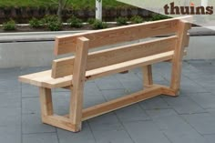 a wooden bench sitting on top of a stone floor next to a park area with trees and bushes in the background