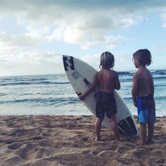 two young boys are standing on the beach with their surfboards looking out at the ocean