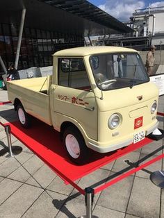 an old yellow truck is on display in front of a red carpeted area and people are looking at it