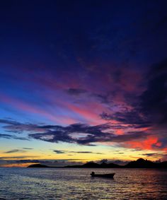 a boat floating on top of a body of water under a colorful sky at sunset