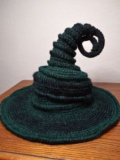 a crocheted green hat sitting on top of a wooden table next to a white wall