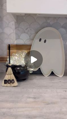 a white ghost sitting on top of a counter next to a black bowl and broom