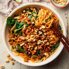 a white bowl filled with noodles, spinach and nuts next to chopsticks