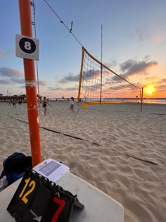 a volleyball net on the beach with people playing volley ball in the background at sunset