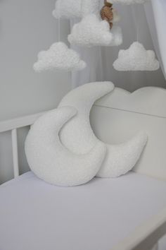 a white crib with a teddy bear hanging from it's side and clouds in the background