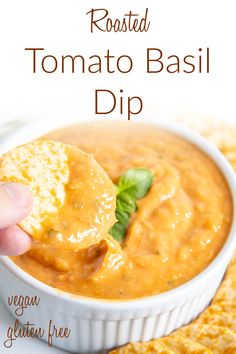 a hand dipping some bread into a bowl of tomato basil dip