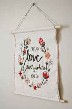 embroidered sign hanging on the wall saying spread love everywhere you go with flowers and hearts