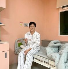 a man in pajamas sitting on a hospital bed holding a piece of paper and smiling