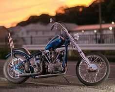 a blue motorcycle is parked on the side of the road at sunset or dawn with houses in the background