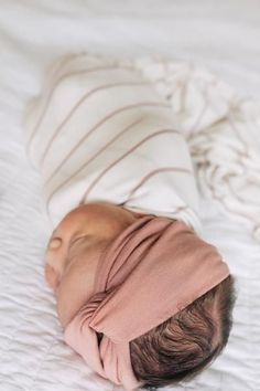 a baby wearing a pink wrap on top of it's head laying on a bed