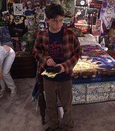 a young man standing in front of a bed with many pictures on the wall behind him