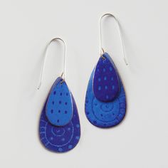 two pairs of blue and white earrings with dots on them, hanging from silver hooks