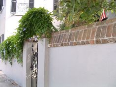 an iron gate with flowers growing over it on the side of a building next to a brick wall